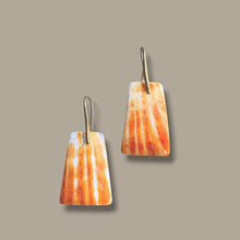 Load image into Gallery viewer, A pair of drop earrings with tapered rectangular pendants featuring a white and orange striped pattern, suspended from thin gold hooks against a solid taupe background.