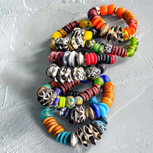 Load image into Gallery viewer, Stack of colorful African beaded bracelets on a textured gray surface