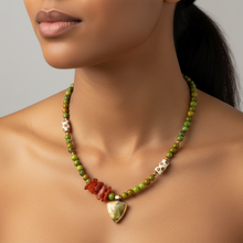 Load image into Gallery viewer, A close-up of a model wearing a handmade beaded necklace. The necklace features olive green and yellow-green beads, a cluster of reddish-orange chips, two white skull beads with black details, and a polished green aventurine heart pendant at the center.