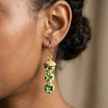 Load image into Gallery viewer, A close-up of a person's ear wearing a dangling earring. The earring has a gold fishhook wire, a small gold bead, and three stacked green and white marbled ring charms with tiny red accents.
