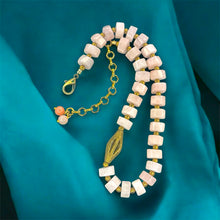 Load image into Gallery viewer, Necklace with pink beads and brass accents on a teal fabric background