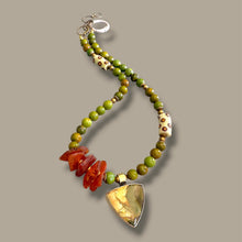 Load image into Gallery viewer, A beaded necklace with green and yellow-green beads, white beads with brown spots, a cluster of orange-red polished stones, and a large triangular yellow-green stone pendant, shown on a plain taupe background.