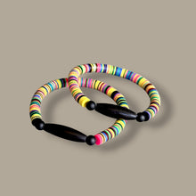 Load image into Gallery viewer, Two colorful beaded bracelets with black wooden toggle clasp, arranged on a solid taupe background.