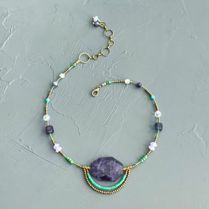 Necklace with beads and a large purple stone on a textured gray background