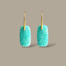 Load image into Gallery viewer, A pair of drop earrings featuring textured turquoise blue-green rectangular pendants with gold-tone hooks, displayed against a solid taupe background.