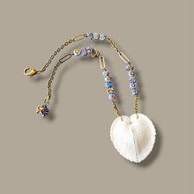 Load image into Gallery viewer, A bohemian-style beaded necklace featuring a large white seashell pendant, gold-toned chain, and blue, yellow, and orange patterned beads, displayed on a solid taupe background.