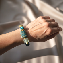 Load image into Gallery viewer, Hand wearing a bracelet with blue and gold beads against a neutral background