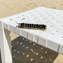 Load image into Gallery viewer, A brass hair barrettes embellished with faceted black spinel sitting on a beach chair on the beach. 