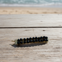 Load image into Gallery viewer, A brass hair barrettes embellished with faceted black spinel sitting on a rock overlooking a beach. 