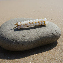 Load image into Gallery viewer, A brass hair  clip embellished with rows of faceted moonstone beads, shown sitting on a rock at the beach.
