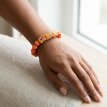Load image into Gallery viewer, A close-up of a person's hand and wrist wearing a beaded bracelet. The bracelet features bright orange round beads alongside a central geometric patterned section in orange, yellow, white, and black.