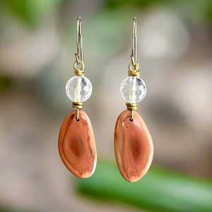 Pair of earrings with peach-colored Imperial Jasper and quartz stones on a blurred natural background