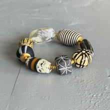 Load image into Gallery viewer, Beaded bracelet with black, white, and gold patterned beads on a gray surface