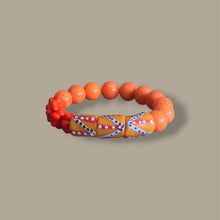 Load image into Gallery viewer, An orange beaded bracelet with a patterned central section, displayed on a solid taupe background.