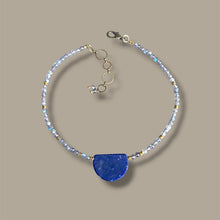 Load image into Gallery viewer, A delicate beaded necklace with labradorite beads, brass spacer accents, and a textured sodalite semicircle pendant, displayed on a solid taupe background.