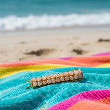 Load image into Gallery viewer, A brass hair barrettes embellished with faceted peach moonstone sitting on a brightly colored beach towel. 