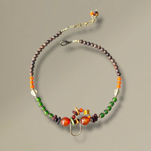 Load image into Gallery viewer, Beaded asymmetrical necklace with green, orange, and brown beads on a tan background