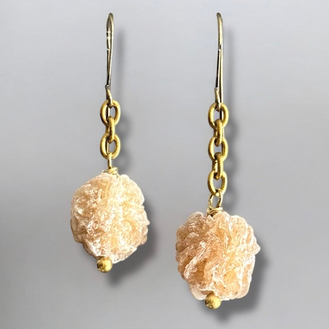 Pair of earrings with gold hooks and beige stone beads on a gray background