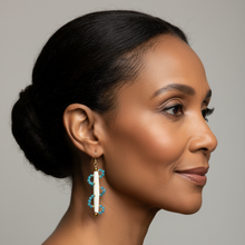 Load image into Gallery viewer, A woman in profile wearing a long drop earring with turquoise blue and white elements, photographed against a plain light gray studio background.