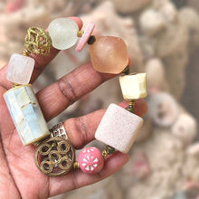 Load image into Gallery viewer, Hand holding a bracelet with various pink and cream beads against a blurred natural background