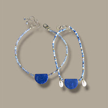 Load image into Gallery viewer, A pair of handmade necklaces with light blue and white beaded strands, featuring a large polished blue semicircle stone and small white teardrop charms, displayed on a solid taupe background.