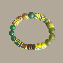 Load image into Gallery viewer, A handmade beaded bracelet featuring green beads, patterned yellow and green cylindrical beads, and a decorative green and gold beaded segment, displayed on a solid taupe background.