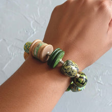 Load image into Gallery viewer, Hand wearing a bracelet with green and brown beads on a light gray background
