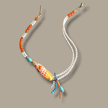 Load image into Gallery viewer, A beaded necklace featuring freshwater white pearl strands, orange coral beads, turquoise accents, and a central patterned orange and white shell-shaped bead, displayed on a solid taupe background.