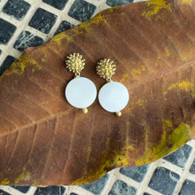 Load image into Gallery viewer, Pair of gold and white earrings on a brown leaf