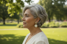 Load image into Gallery viewer, Pair of gold and white earrings on a brown leaf