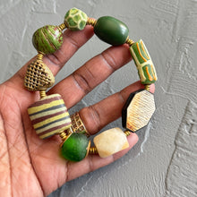 Load image into Gallery viewer, Hand holding a green and cream beaded bracelet against a gray background