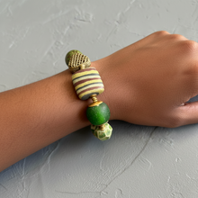 Load image into Gallery viewer, Hand wearing a bracelet with green and gold beads on a gray background