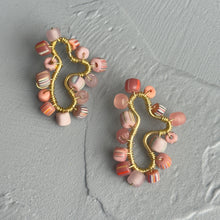 Load image into Gallery viewer, A pair of handmade wire-wrapped earrings with pink, peach, and striped glass beads, displayed on a textured gray stone surface.