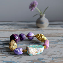 Load image into Gallery viewer, Bracelet with purple and gold beads on a textured surface with a vase and flower in the background