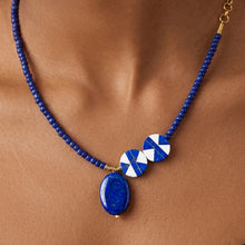 Load image into Gallery viewer, A close-up of a beaded necklace worn on a model's neck, featuring a blue stone pendant, two blue and white patterned round beads, and gold-toned accents.