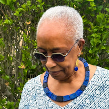 Load image into Gallery viewer, Woman wearing sunglasses and a blue necklace with a green leafy background