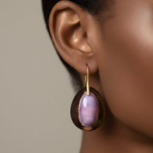 Load image into Gallery viewer, A close-up of a model's ear wearing a large oval purple and brown cowrie shell earring. 