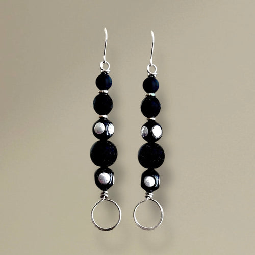 Black beaded earrings with silver loops on a beige background