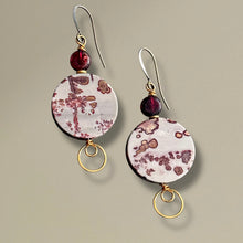 Load image into Gallery viewer, Pair of earrings with circular designs and red beads on a beige background
