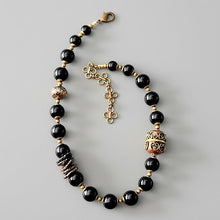 Load image into Gallery viewer, Black beaded necklace with brass and copper accents on a gray background
