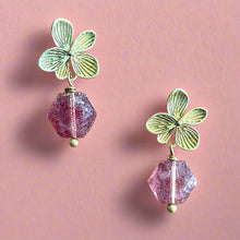 Load image into Gallery viewer, Pair of earrings with green leaf-like tops and pink gemstones on a pink background