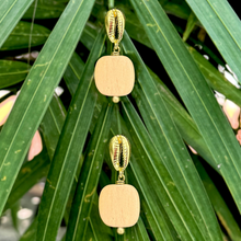 Load image into Gallery viewer, Pair of earrings with gold and beige beads against a green leafy background