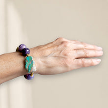 Load image into Gallery viewer, Hand wearing a bracelet with purple and green beads on a plain background
