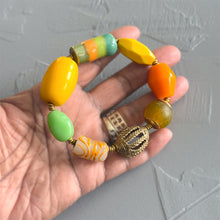 Load image into Gallery viewer, Hand holding a colorful beaded bracelet with a gold clasp against a gray background