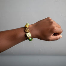 Load image into Gallery viewer, Hand wearing a bracelet with green and gold beads on a gray background