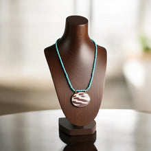 Load image into Gallery viewer, Necklace with a large circular pendant on a wooden mannequin bust against a blurred background