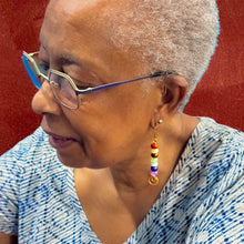 Load image into Gallery viewer, Woman wearing glasses and colorful earrings against a red background