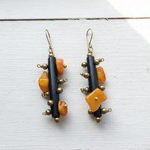 Load image into Gallery viewer, Pair of earrings with black, orange, and gold beads on a white wooden surface