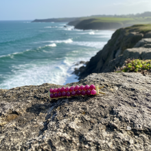 Load image into Gallery viewer, A brass hair barrettes embellished with faceted rubies sitting on a rock overlooking a beach. 