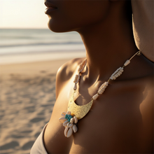 Load image into Gallery viewer, A close-up lifestyle shot of a woman on a beach wearing a bohemian crescent moon necklace made of brass, white seashells, and turquoise beads.